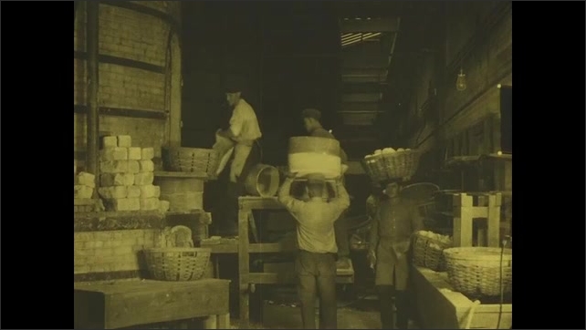 1910s: Men climbing ladders to stack pottery in kiln. Men moving baskets of pottery on their heads. Workers removing cups from bath and arranging on planks.