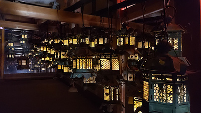 A row of lit lanterns hung underneath part of a large shrine.