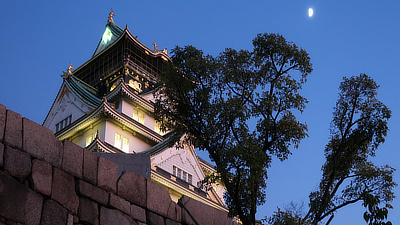 Osaka Castle with the moon in the sky.