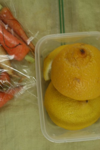 A close up of two half lemons and a lemon wedge in a plastic container. To their left is a baggie of carrots.