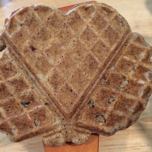 A close up of a heart-shaped waffle, with a couple blobs of waffle that didn't manage to become heart-shaped on each side.