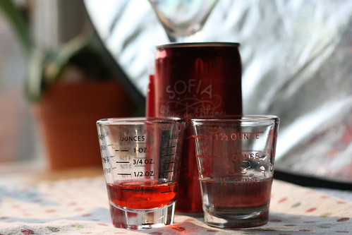 A can of Sofia Blanc de Blancs with a partially full shot glass of red liquid and one of clear liquid.