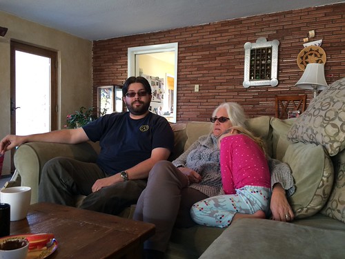 Three people sitting on a couch together; a male, older female, and a child cuddled up to the older female. Only the male is looking at the camera. Everyone looks relaxed.