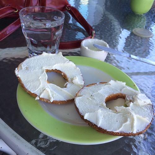 A photo of a bagel spread with cream cheese. A glass of water next to it.